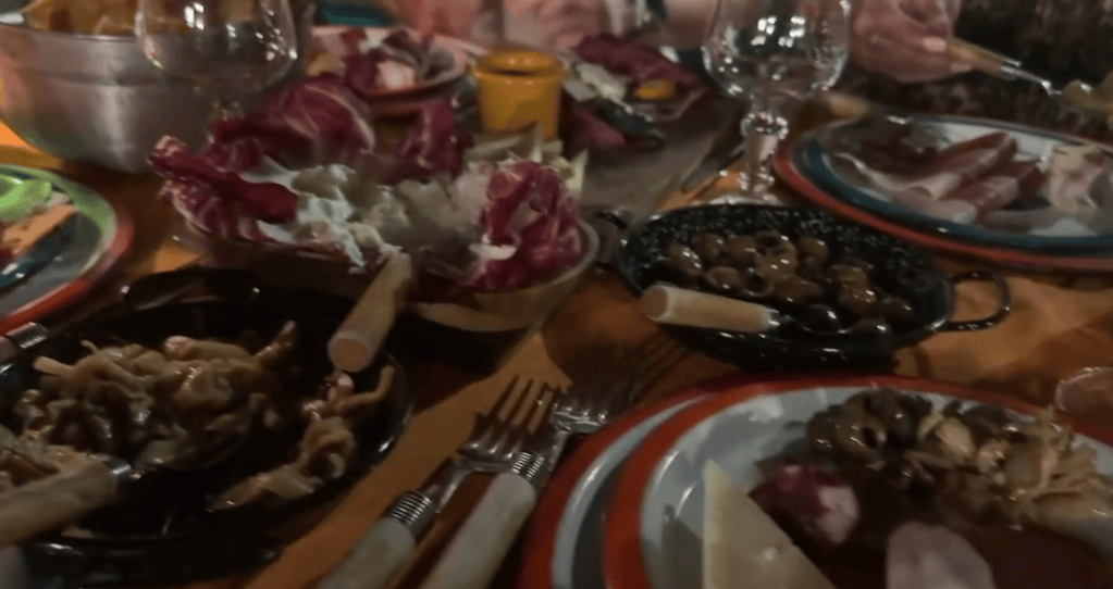 A dining table set with various dishes, including salads, olives, and a variety of meats, with utensils and glassware visible.