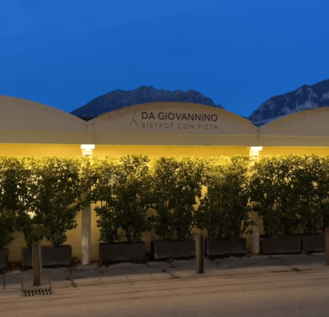 Exterior view of Da Giovannino Bistrot con Pizza at night, featuring a lit sign and greenery along the establishment.