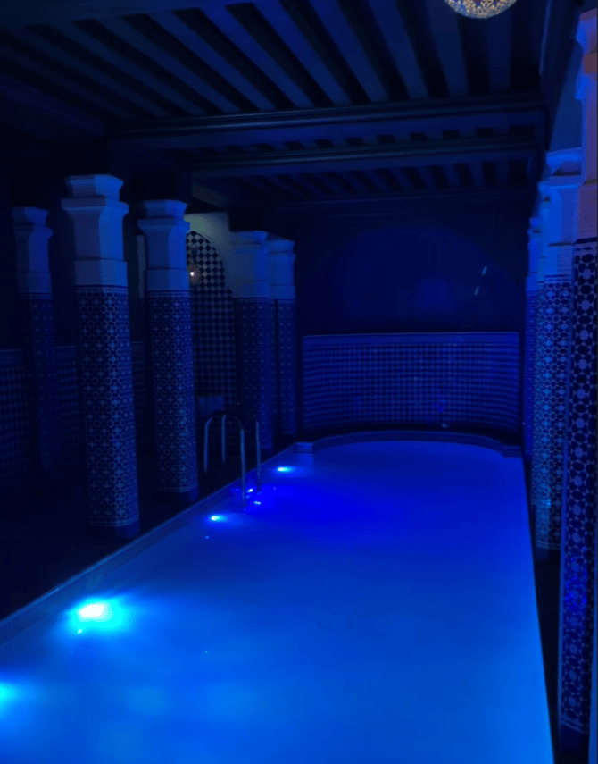 Indoor swimming pool illuminated with blue lights, surrounded by decorative tiled columns and a stylish ceiling.